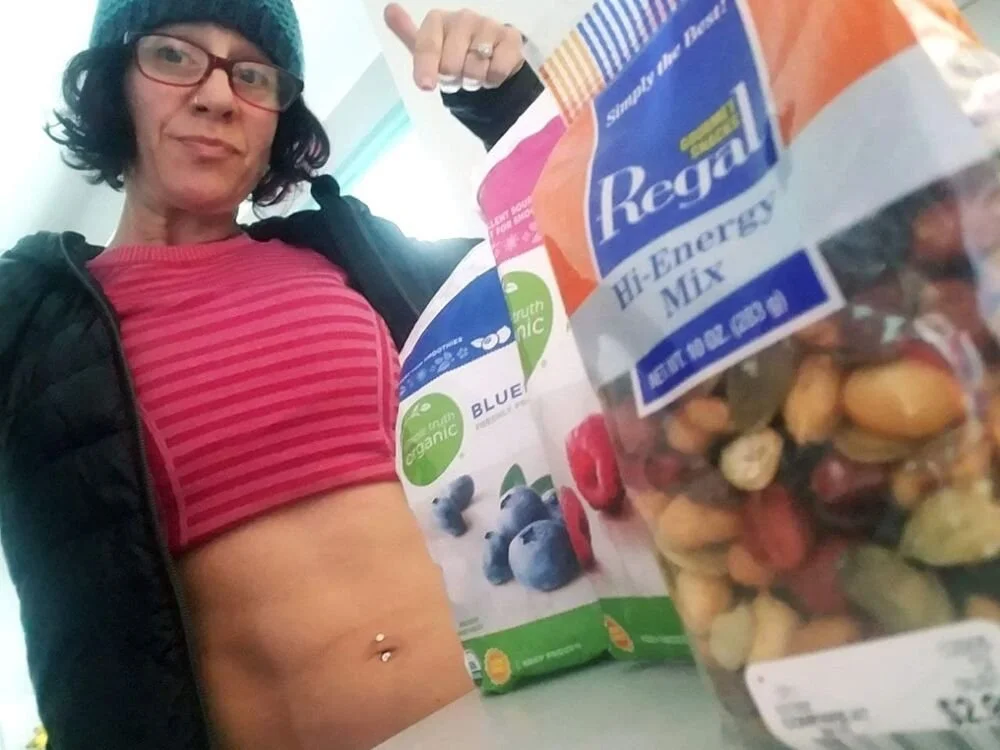 A client smiling beside a table of fresh food and pantry staples